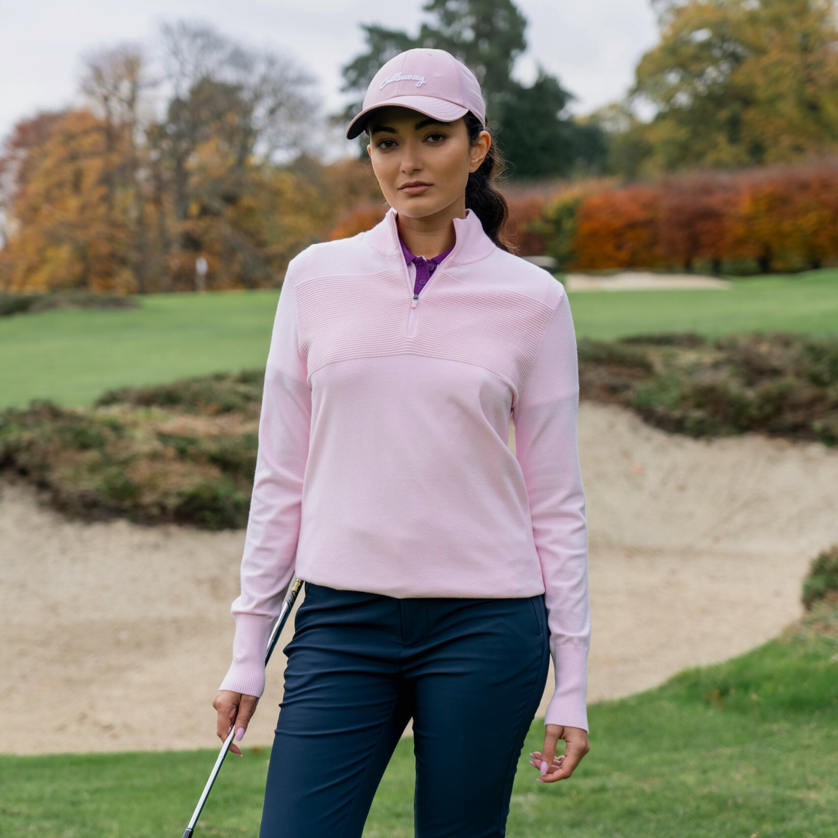 Female golfer wearing the Callaway Soft Stretch Zip-Neck Sweater in Cherry Blossom on the golf course
